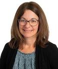 Headshot: Dark haired woman with Glasses in Dark suit Jacket and Grey top